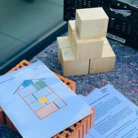 Anleitung für Insektenhotelbau liegt auf einem Tisch auf Ziegelsteinen, Holzmaterialien liegen daneben