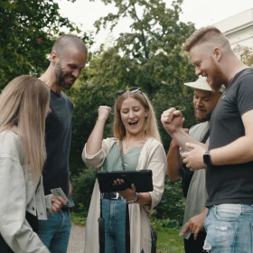 Eine Gruppe von Menschen schaut auf ein Tablet und jubelt.