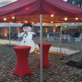 zwei Stehtische vor einer Eisstockbahn mit einem aufblasbaren Schneemann