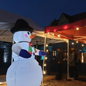 Schneemann vor der Eisstockbahn und einem roten Pavillion mit Lichterkette