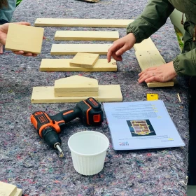 Bausatz für ein Insektenhotel liegt auf einem Tisch verteilt, Akkuschrauber und Anleitung liegen daneben