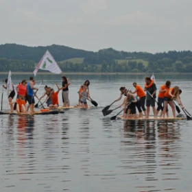 Zwei Flöße auf dem Wasser. Jeweils 6 Personen auf jedem Floß. Flöße fahren auf einem See