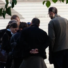 7 Personen stehen in einem Kreis und schauen gemeinsam auf ein Tablet