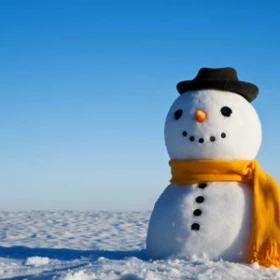 Schneemann auf einer verschneiten Fläche, der Schneemann trägt einen gelben Schaal und einen schwarzen Hut