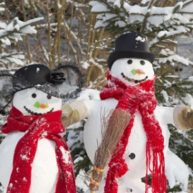 zwei Schneemänner mit rotem Schaal stehen nebeneinander vor einem Nadelwald