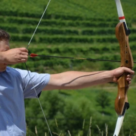 EVINTA_Teamski_Sommerbiathlon_Bild 01 Eine Person steht seitlich und hat Pfeil und Bogen gespannt