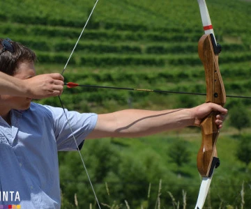EVINTA_Teamski_Sommerbiathlon_Bild 01 Eine Person steht seitlich und hat Pfeil und Bogen gespannt