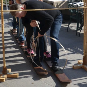 Vier Personen meistern gemeinsam die Teamski-Challenge und bewegen sich unter einer Limbo-Stange hindurch – ein lustiges Outdoor-Teamevent für Teamwork und Spaß.