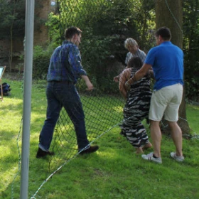 Ein Netz ist senkrecht gespannt. Vier Personen stehen um das Netz. Eine Person ist gerade durch ein großes Loch im Netz geklettert.