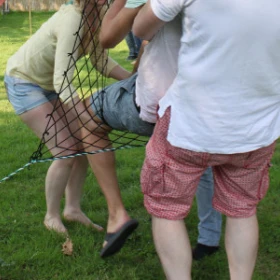 EVINTA_Teamspiel_Teamnettz_Bild 05 Zwei Personen versuchen eine dritte Person nur ein Loch in einem Netzt zu befördern.
