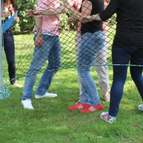 EVINTA_Teamspiel_Teamnettz_Bild 06 Vier Personen stehen vor einem Netz. Das Netz hat ein Loch.