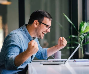 Mann schaut auf einen Laptop und jubelt