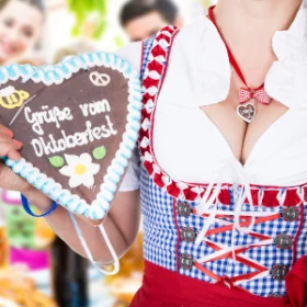 Eine Frau im Dirndl fällt ein Lebkuchenherz mit der Aufschrift "Grüße vom Oktoberfest" in die Kamera