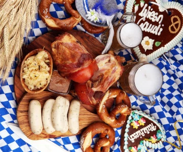 ein festlich dekorierter Tisch mit bayrischen Spezialitäten, verschiedene Würste, Salzbrezeln, Lebkuchenherzen, bayrische Dekoration