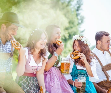Personen in bayrischer Tracht feiern, trinken Bier und essen Brezeln