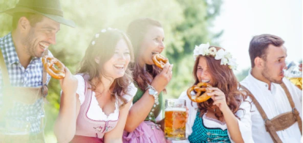 Personen in bayrischer Tracht feiern, trinken Bier und essen Brezeln