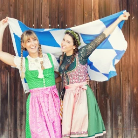 Zwei Frauen in bayrischer Tracht mit Bayrischer Flagge vor einem Holztor
