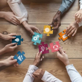 Hände halten Puzzleteile in die Mitte eines Tisches zusammen