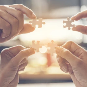 Vier Hände halten Puzzleteile in die Luft