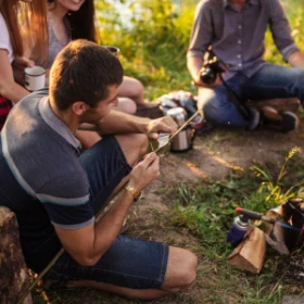 Gruppe von Menschen sitz auf dem Waldboden und macht Feuer