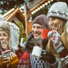 Menschen mit Mütze und Schal trinken Glühwein zusammen und lachen