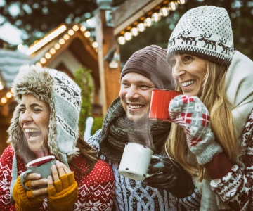 Menschen mit Mütze und Schal trinken Glühwein zusammen und lachen