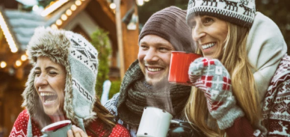 Menschen mit Mütze und Schal trinken Glühwein zusammen und lachen