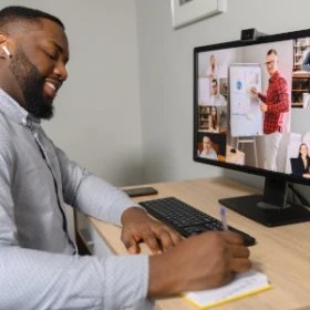 Mann freut sich und macht sich Notizen vor seinem Rechner