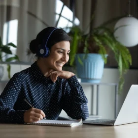 Frau mit Headset freut sich und sitzt vor ihrem Laptop