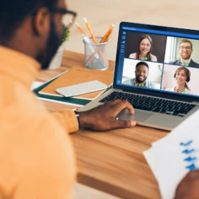 Mann vor einem Laptop auf einem Schreibt, führt ein Meeting durch