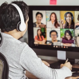 Mann sitzt mit einem Headset am Schreibtiach und hört einem Meeting zu