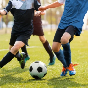 3 Personen laufen um einen Fußball herum