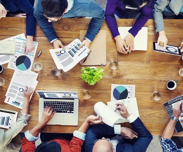 Personen sitzen zu einem Meeting gemeinsam an einem Holztisch und analysieren Statistiken