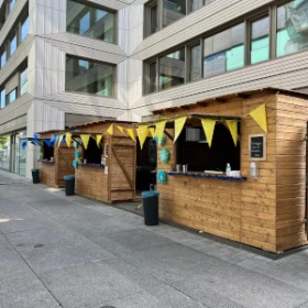 bunt geschmückte Markthütten in einer Stadt vor einem Bürohaus, blaue und gelbe Wimpelkette, Hütte aus Holz