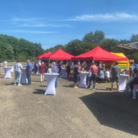 rote Pavillons und weiße Stehtische als Markt, viele Menschen, Marktatmosphäre, im Hintergrund Hüpfburg für Kinder