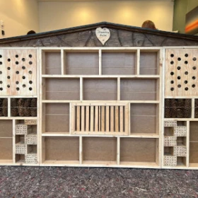 Rohbau eines großen Insektenhotels mit Dach, einige Fächer sind schon gefüllt mit Holz, Zielsteinen und Stroh