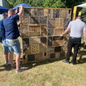 großes Insektenhotel, 2 Meter hoch und 2 Meter breit, 2 Männer halten das Insektenhotel