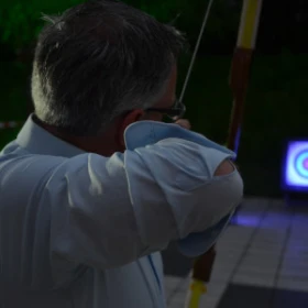 Person von hinten beim schießen mit einem Bogen auf eine beleuchtete Zielscheibe bei Nacht