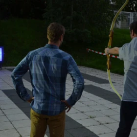 Person spannt den Bogen zum Bogenschießen, eine weitere Person schaut zu