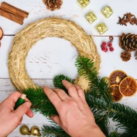 Adventskranz Rohling aus Stroh wird mit Tannengrün verziert, Dekorationselemente aus Tanne und getrockneten Früchten liegen daneben