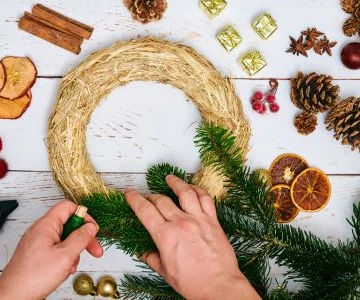 Adventskranz Rohling aus Stroh wird mit Tannengrün verziert, Dekorationselemente aus Tanne und getrockneten Früchten liegen daneben