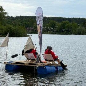 Floß auf einem See, 2 Personen sitzen im Liegestuhl auf dem Floß