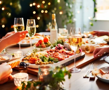 Weihnachtstafel mit frischem Essen, Weingläser, im Hintergrund Weihnachtsbaum mit Lichtern