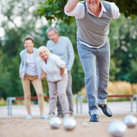 Mann wirft Boule Kurgel, im Hintergrund schauen 3 Personen zu
