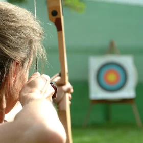 Frau zielt mit Bogen auf Zielscheibe