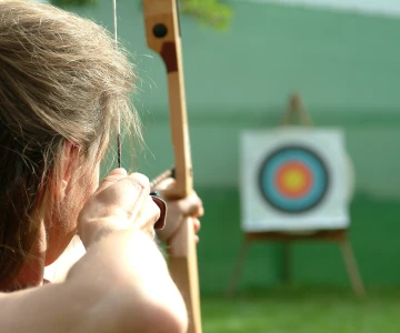 Frau zielt mit Bogen auf Zielscheibe