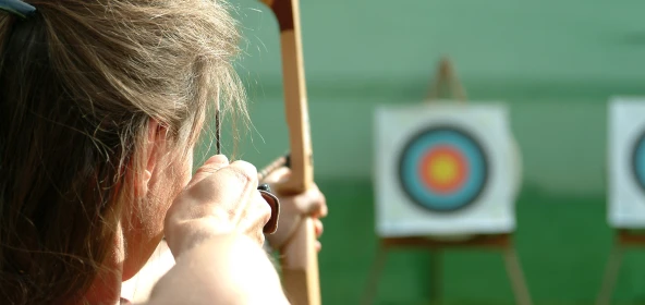Frau zielt mit Bogen auf Zielscheibe