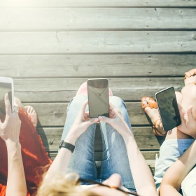 mehrere Personen sitzen auf einer Bank und haben ein Handy in der Hand