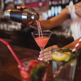 Cocktail wird aus Shaker ins Martiniglas gegossen