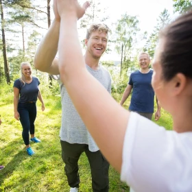 Gruppe von Menschen auf einer Wiese im Wald, zwei Personen klatschen ab